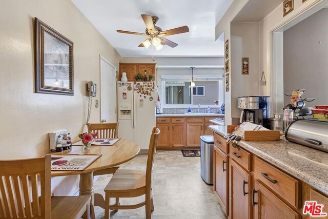 kitchen featuring ceiling fan, light stone countertops, white refrigerator with ice dispenser, and sink