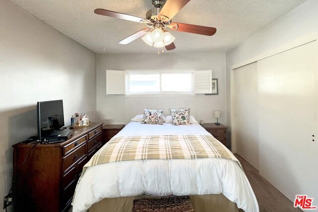 carpeted bedroom with ceiling fan, a closet, and a textured ceiling