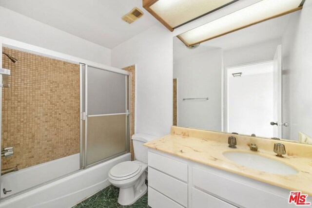 full bathroom with combined bath / shower with glass door, vanity, and toilet