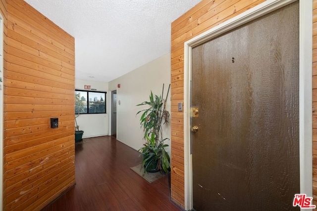 hall featuring a textured ceiling, dark wood-type flooring, and wood walls