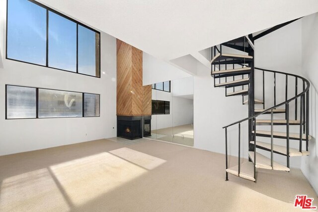 unfurnished living room featuring carpet flooring, a multi sided fireplace, and a high ceiling