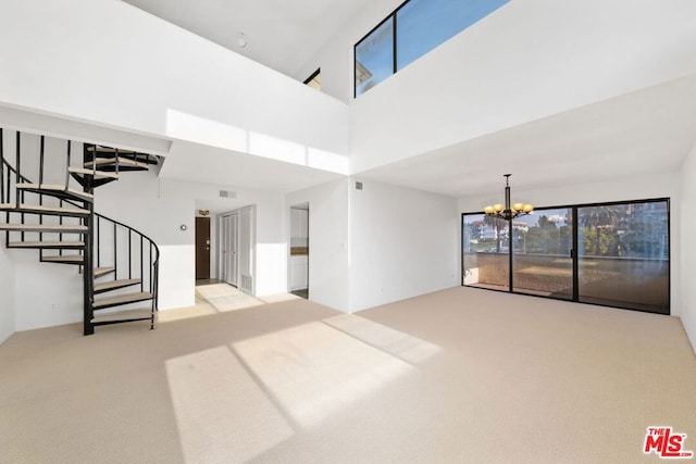 unfurnished living room featuring a high ceiling, light colored carpet, and a chandelier