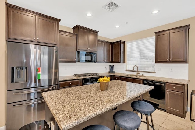 kitchen featuring a kitchen island, a breakfast bar, sink, stainless steel appliances, and light stone counters