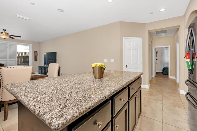 kitchen featuring ceiling fan, a kitchen island, stainless steel refrigerator, light tile patterned flooring, and light stone countertops