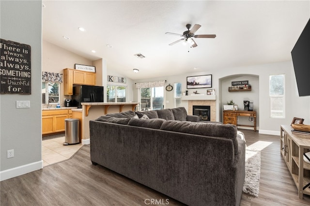 living room featuring lofted ceiling, a fireplace, sink, ceiling fan, and light hardwood / wood-style flooring