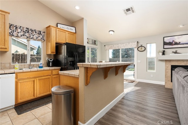 kitchen with dishwasher, a tile fireplace, black refrigerator with ice dispenser, sink, and tile counters