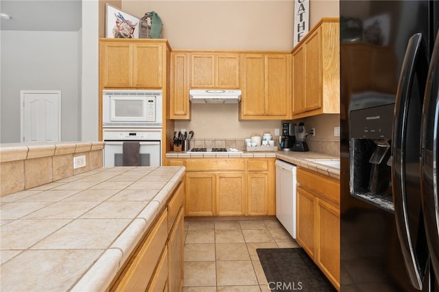 kitchen with light tile patterned flooring, tile counters, light brown cabinetry, and white appliances