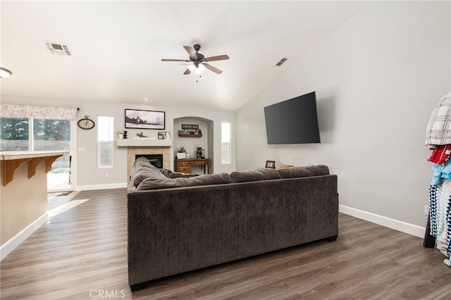 living room featuring ceiling fan, a tiled fireplace, lofted ceiling, and wood-type flooring