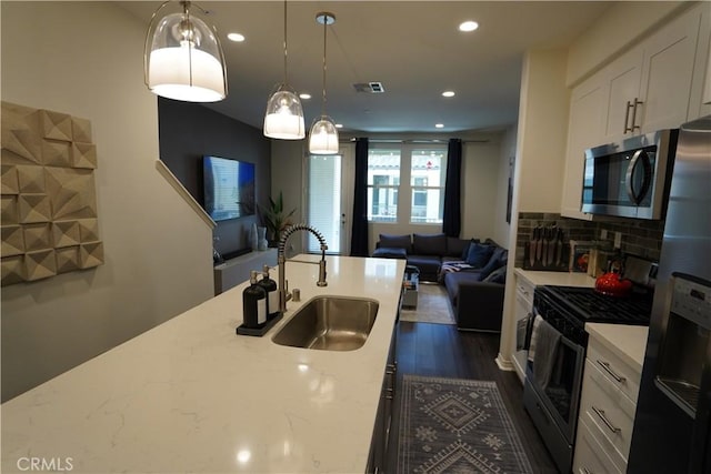 kitchen with pendant lighting, appliances with stainless steel finishes, white cabinets, sink, and light stone counters