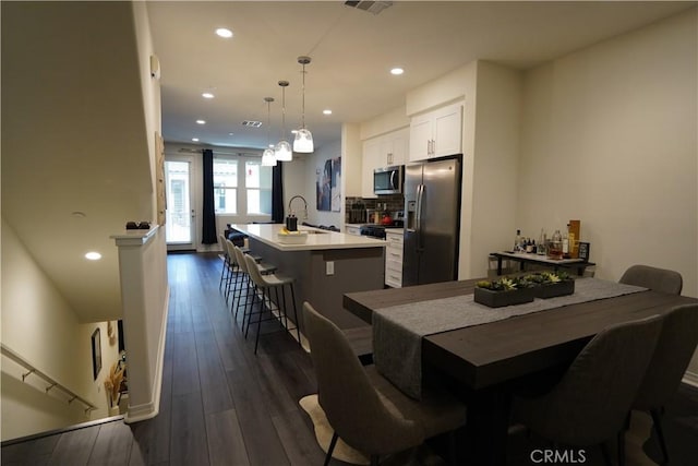 kitchen with a kitchen bar, stainless steel appliances, a kitchen island with sink, pendant lighting, and white cabinets