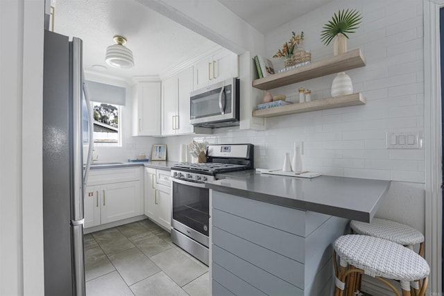 kitchen with light tile patterned floors, stainless steel appliances, tasteful backsplash, a kitchen breakfast bar, and white cabinets