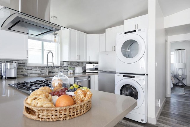 kitchen featuring stacked washing maching and dryer, white cabinetry, decorative backsplash, and appliances with stainless steel finishes