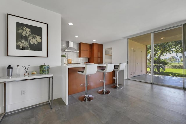 kitchen featuring backsplash, a kitchen breakfast bar, expansive windows, kitchen peninsula, and wall chimney exhaust hood