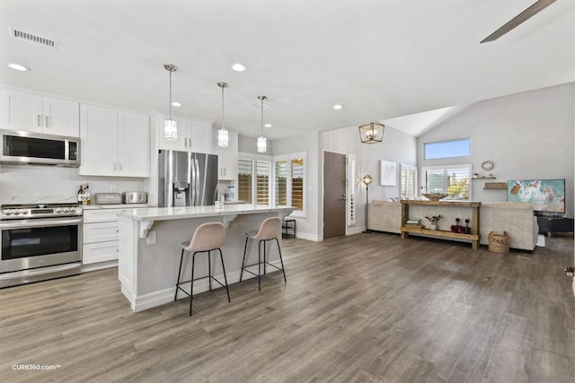 kitchen featuring a kitchen bar, a center island with sink, stainless steel appliances, hanging light fixtures, and white cabinets