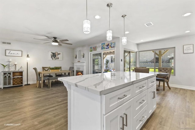 kitchen featuring white cabinets, a center island, hanging light fixtures, ceiling fan, and light stone counters