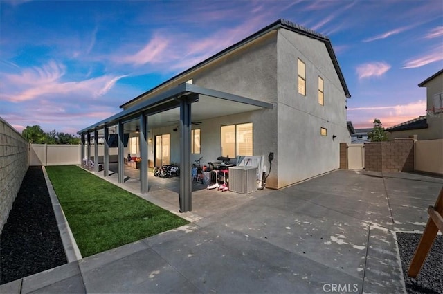 back house at dusk with ceiling fan and a patio area