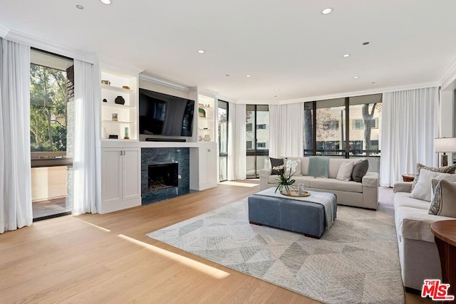 living room featuring light wood-type flooring, a high end fireplace, a wealth of natural light, and crown molding