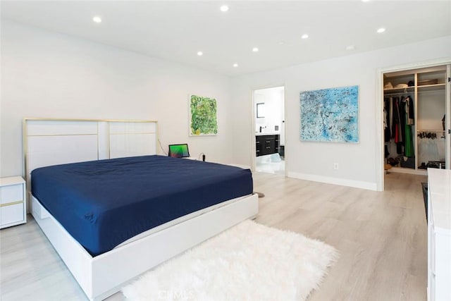 bedroom featuring ensuite bath, a walk in closet, a closet, and light hardwood / wood-style flooring