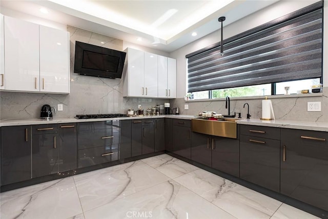 kitchen with white cabinetry, decorative backsplash, hanging light fixtures, and sink