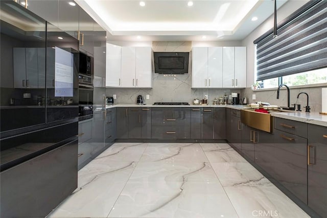 kitchen featuring tasteful backsplash, a raised ceiling, sink, light stone countertops, and white cabinets