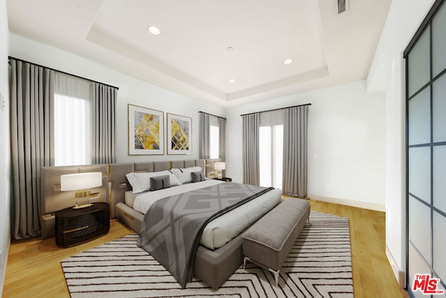 bedroom with light hardwood / wood-style floors and a tray ceiling