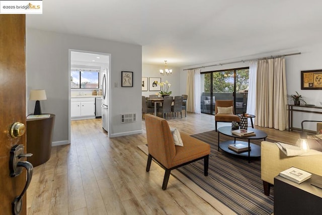 living room featuring an inviting chandelier, light hardwood / wood-style flooring, and a wealth of natural light