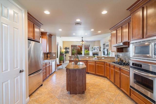 kitchen featuring light stone countertops, appliances with stainless steel finishes, a center island, tasteful backsplash, and kitchen peninsula