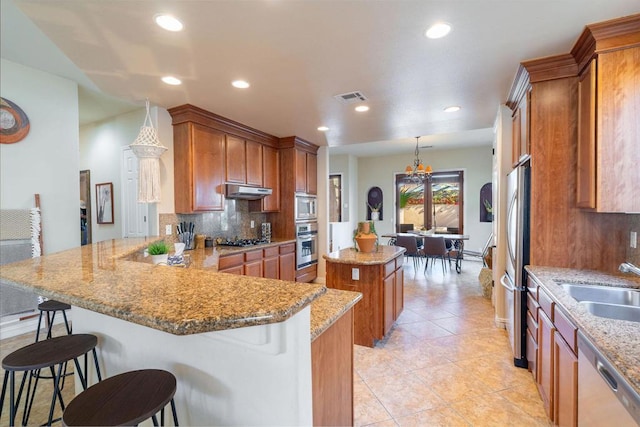 kitchen with pendant lighting, stainless steel appliances, tasteful backsplash, a kitchen breakfast bar, and kitchen peninsula