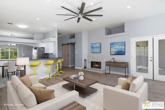 living room with ceiling fan with notable chandelier, french doors, sink, light hardwood / wood-style flooring, and a barn door