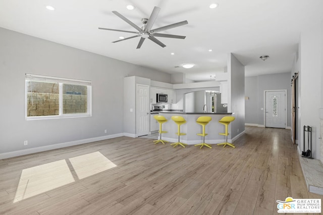 kitchen with a barn door, stainless steel appliances, white cabinets, light hardwood / wood-style flooring, and a breakfast bar