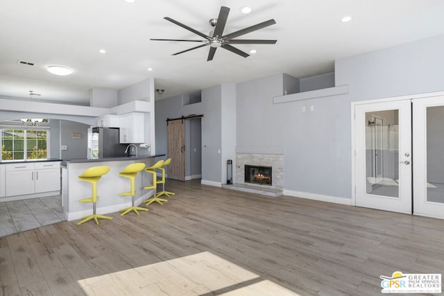 kitchen with a kitchen bar, white cabinetry, light hardwood / wood-style floors, stainless steel fridge, and a barn door