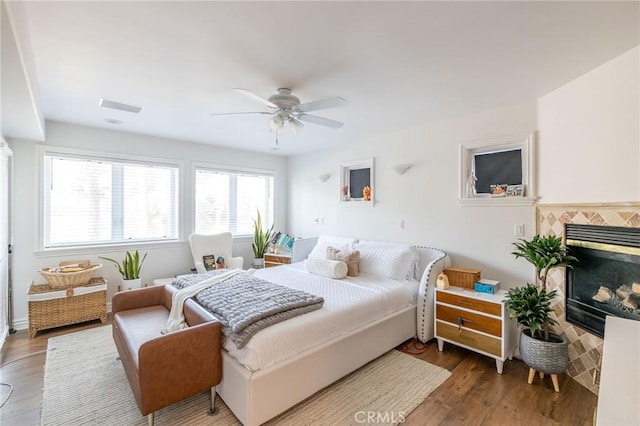 bedroom featuring ceiling fan, hardwood / wood-style flooring, and a tile fireplace