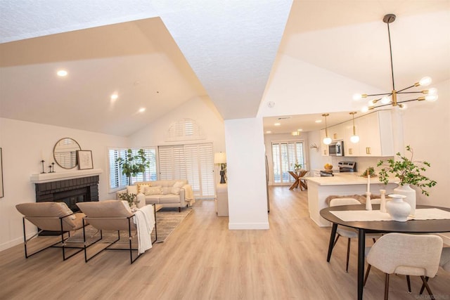 living room with an inviting chandelier, a fireplace, high vaulted ceiling, and light hardwood / wood-style flooring