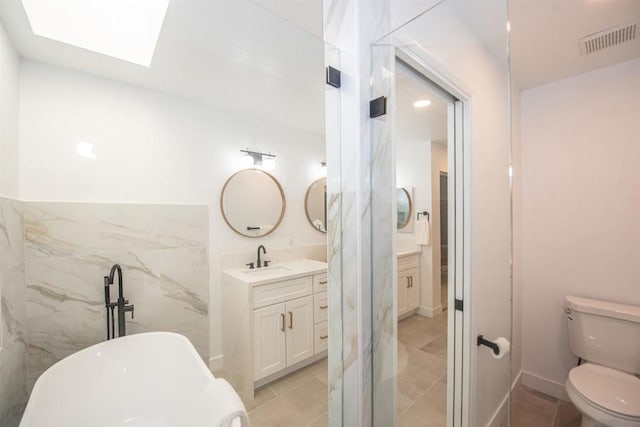 bathroom featuring a skylight, vanity, toilet, and a tub to relax in