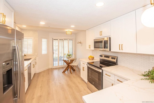 kitchen with white cabinetry, light stone counters, stainless steel appliances, and light hardwood / wood-style floors