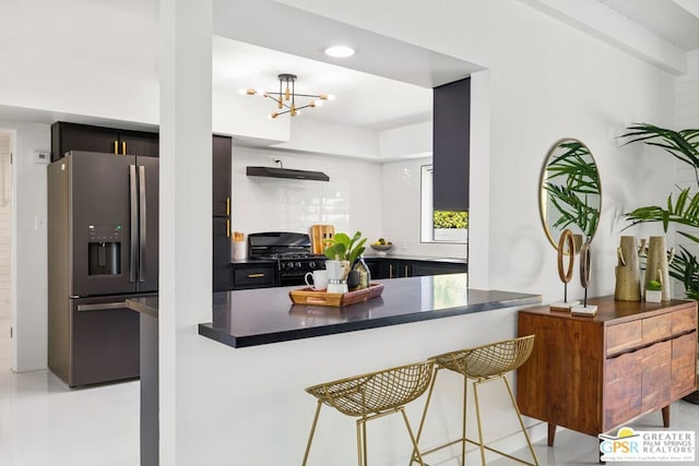 kitchen featuring stainless steel fridge, black range with gas cooktop, a notable chandelier, ventilation hood, and kitchen peninsula