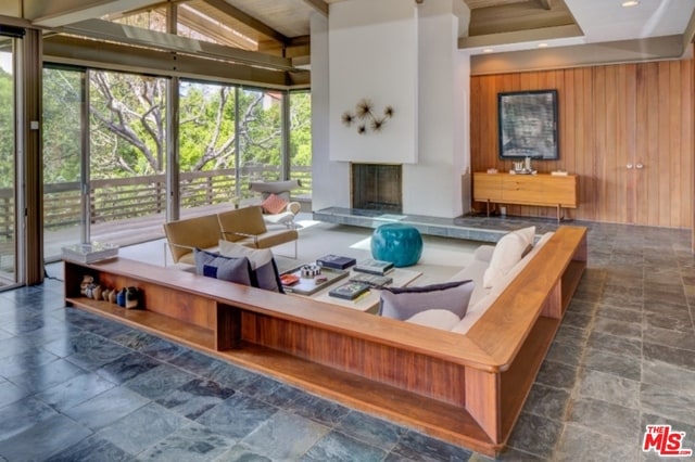 living room featuring plenty of natural light, wood walls, a tiled fireplace, and vaulted ceiling with beams