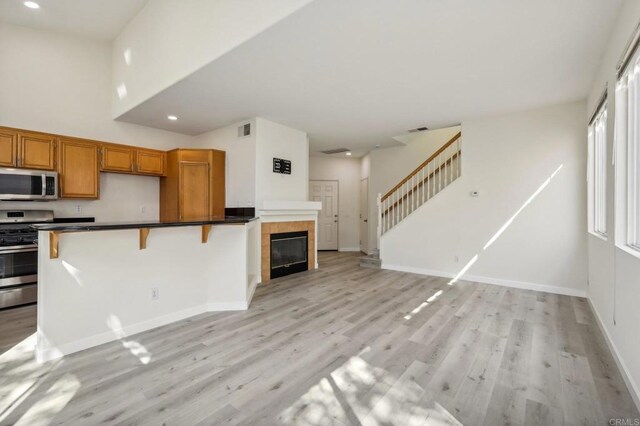 kitchen featuring appliances with stainless steel finishes, light hardwood / wood-style floors, a kitchen bar, and a tiled fireplace