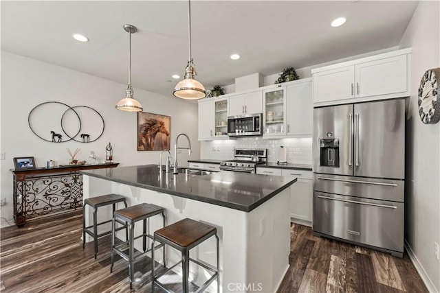 kitchen with white cabinets, backsplash, appliances with stainless steel finishes, and a center island with sink