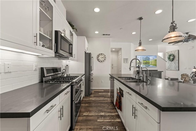 kitchen with white cabinets, hanging light fixtures, appliances with stainless steel finishes, and a kitchen island with sink