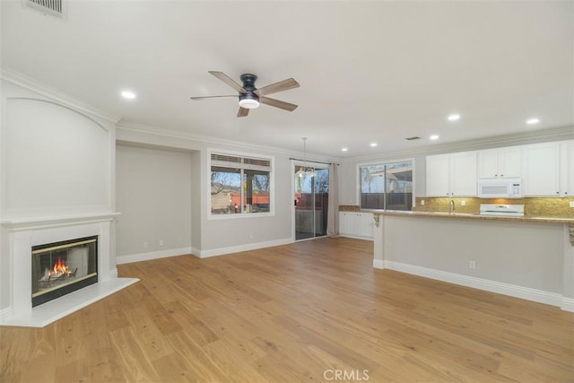 unfurnished living room featuring ceiling fan, ornamental molding, sink, and light wood-type flooring