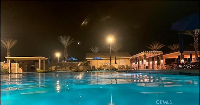 pool at night featuring a pergola and a patio