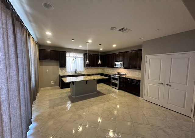 kitchen featuring sink, stainless steel appliances, light stone counters, a kitchen island, and decorative light fixtures