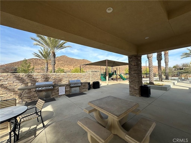 view of patio / terrace featuring an outdoor kitchen, a playground, area for grilling, and a mountain view