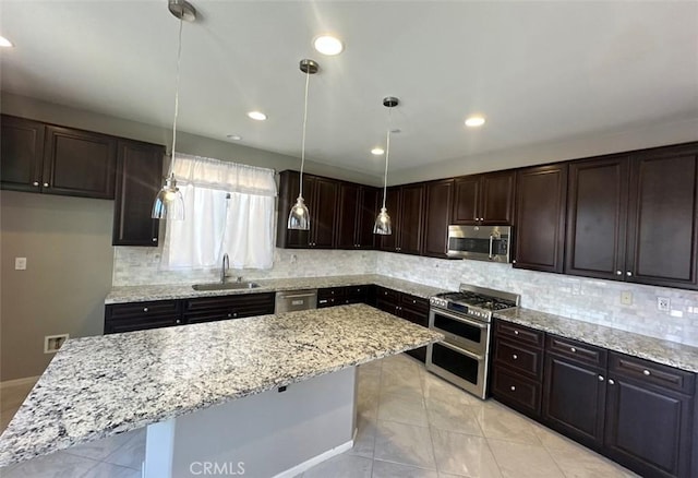 kitchen featuring pendant lighting, sink, appliances with stainless steel finishes, dark brown cabinets, and a center island