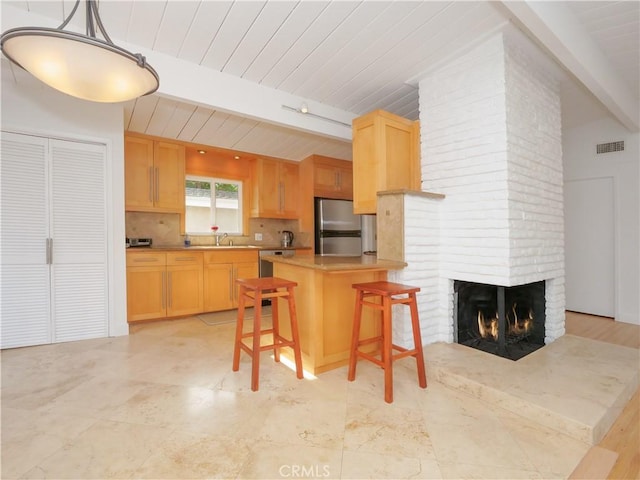 kitchen featuring kitchen peninsula, appliances with stainless steel finishes, decorative light fixtures, a kitchen breakfast bar, and a fireplace