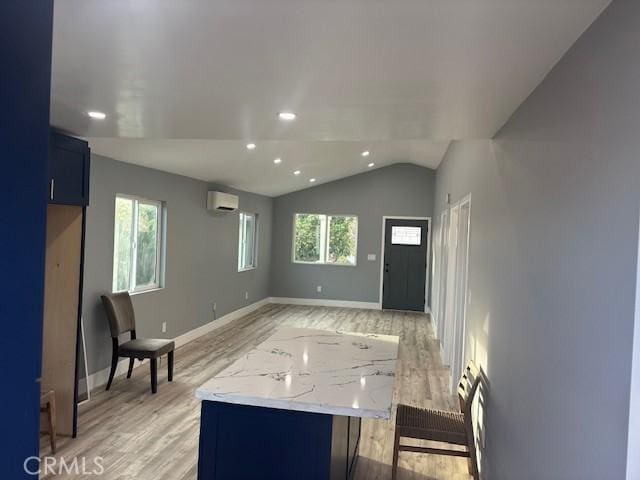 interior space featuring vaulted ceiling, a wall mounted AC, light hardwood / wood-style floors, and plenty of natural light