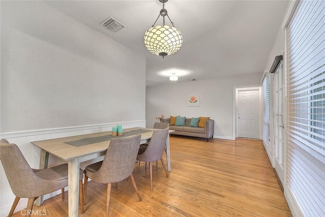 dining space with a wainscoted wall, visible vents, and light wood-style flooring