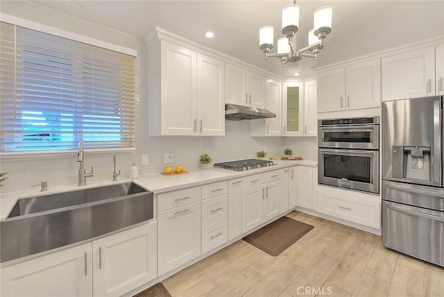 kitchen featuring appliances with stainless steel finishes, hanging light fixtures, light countertops, under cabinet range hood, and a sink