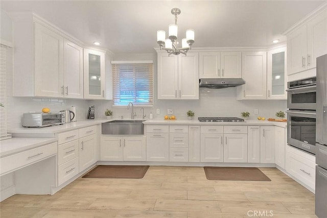 kitchen with appliances with stainless steel finishes, light countertops, under cabinet range hood, white cabinetry, and a sink